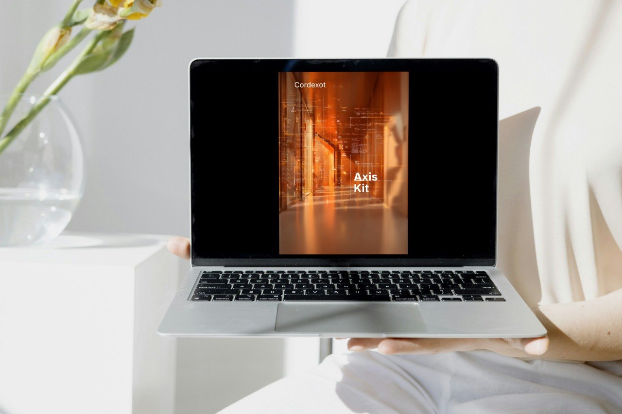 Laptop displaying a design software interface on a white surface with a vase of flowers.
