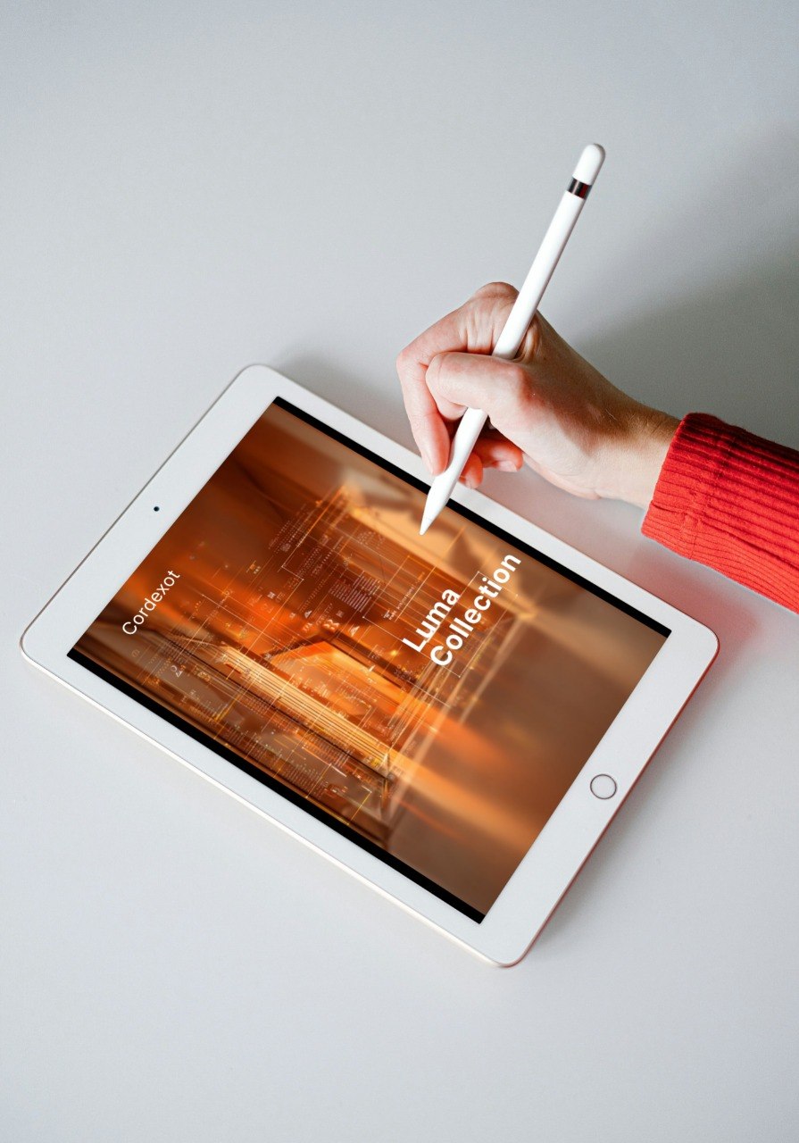 Hand holding a stylus over an iPad displaying a 'Luna Collection' image on a light gray background